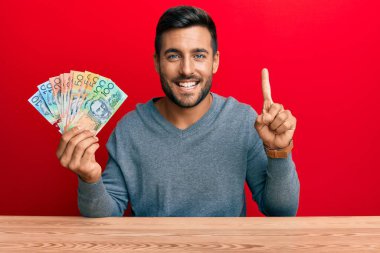 Avustralya doları tutan yakışıklı İspanyol bir adam bir fikirle gülümsüyor ya da bir soru işareti yapıyor, bir numara: 