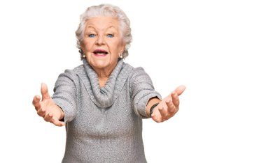 Kış süveteri giyen yaşlı gri saçlı kadın kameraya sarılıp gülümsüyor. Mutluluğu kucaklayan neşeli bir ifade.. 