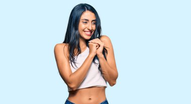 Güzel İspanyol kadın sıradan kıyafetler giyiyor. Gergin ve heyecanlı bir şekilde gülüyor. Elleri çenesinde yan tarafa bakıyor. 