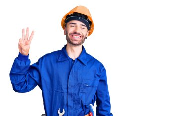 İspanyol işçi üniforması giyen genç adam üç numarayı gösterip işaret ederken kendinden emin ve mutlu gülümsüyor.. 