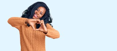 Güzel Afro-Amerikalı kadın, sıradan bir süveter giyip, aşıkken gülümsüyor, elleriyle kalp sembolü yapıyor. romantik kavram. 