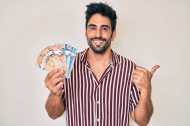 Yakışıklı, sakallı, Kanada doları tutan ve ağzı açık gülümseyen bir İspanyol. 