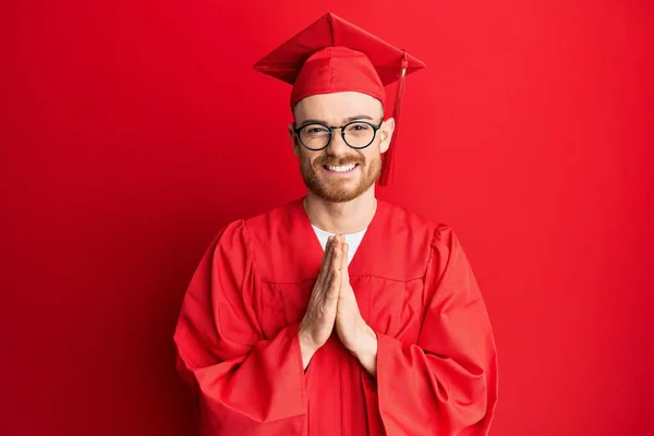 Νεαρός Κοκκινομάλλης Φοράει Κόκκινο Καπέλο Αποφοίτησης Και Επίσημη Ρόμπα Προσεύχεται — Φωτογραφία Αρχείου