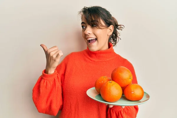 Mujer Hispana Joven Sosteniendo Naranjas Frescas Apuntando Con Pulgar Hacia —  Fotos de Stock