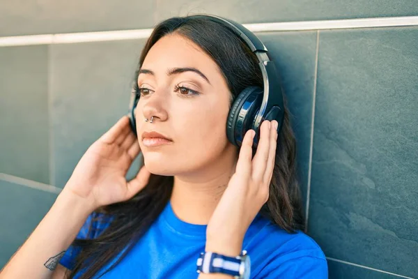 街でヘッドフォンを使用して音楽を聴く真剣な表情の若いヒスパニック系女性 — ストック写真