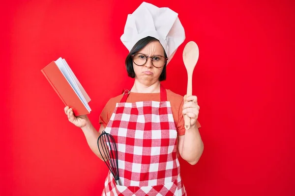 Brünette Frau Mit Syndrom Trägt Professionelle Bäckerschürze Liest Kochrezeptbuch Deprimiert — Stockfoto