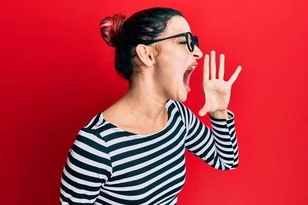 Young caucasian woman wearing casual clothes and glasses shouting and screaming loud to side with hand on mouth. communication concept.