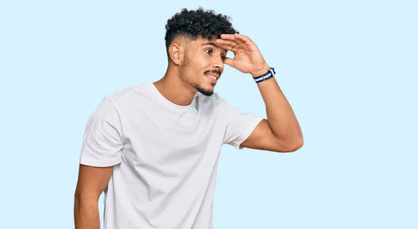 若いアラブ人の男性は非常に幸せと笑みを浮かべて遠くに手を頭の上に見てカジュアルな白いTシャツを着て 検索の概念 — ストック写真