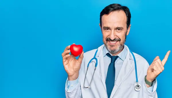 Średniego Wieku Przystojny Kardiolog Mężczyzna Nosi Stetoskop Trzymając Plastikowe Serce — Zdjęcie stockowe