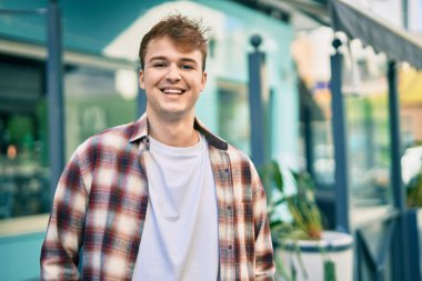 Genç beyaz adam gülümseyerek şehirde mutlu mesut duruyor..