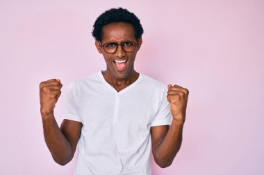 Sıradan kıyafetler ve gözlük takan Afrikalı yakışıklı adam gururla bağırıyor, zaferi kutluyor ve başarıyı kollarını kaldırarak kutluyor. 