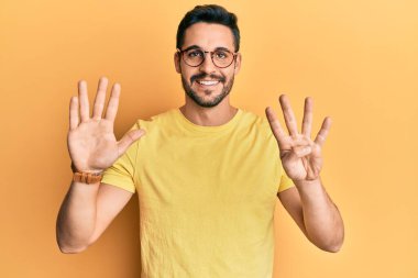 Gündelik kıyafetler giyen ve gözlük takan İspanyol genç adam dokuz numarayı gösterip işaret ederken kendinden emin ve mutlu bir şekilde gülümsüyor.. 