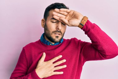 Günlük kıyafetler giyen genç İspanyol adam hastalık, ateş, grip ve virüs için alnına dokunuyor. 