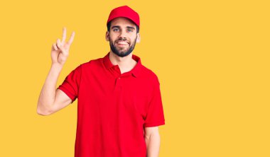 Sakallı, teslimat üniforması giyen, gülümseyen ve parmaklarını zafer işareti yapan genç yakışıklı bir adam. İki numara.. 