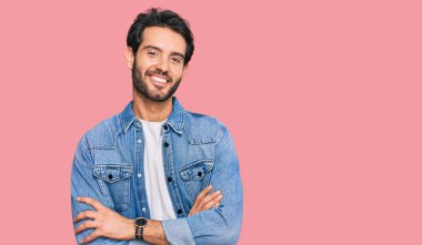 Gündelik kıyafetler giyen, kollarını kavuşturup kameraya gülümseyen genç İspanyol adam. pozitif kişi. 