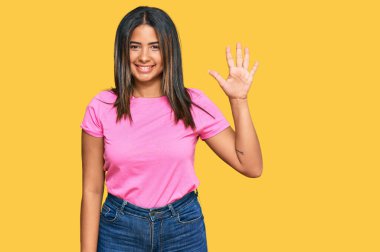 Gündelik giysiler giyen genç Latin kız beş numarayı gösterip işaret ederken kendinden emin ve mutlu bir şekilde gülümsüyor.. 