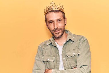 Kral tacı takan yakışıklı genç adam kollarını kavuşturup kameraya bakıyor. pozitif kişi. 
