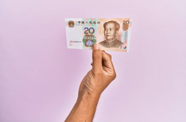 Hispanik el 20 Yuan 'lık Çin banknotunu soyutlanmış pembe arka planda tutuyor.