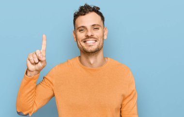 Gündelik kıyafetler giyen genç İspanyol bir numarayı gösterip işaret ederken kendinden emin ve mutlu bir şekilde gülümsüyor.. 