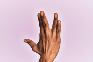 Siyah orta yaşlı bir kadının kolu ve eli pembe izole edilmiş arka planda Vulkan selamı veriyor, elinin ve parmaklarının tersini gösteriyor, ucube kültürü sergiliyor. 
