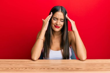 Genç İspanyol kadın, gündelik giysiler giyip masada oturuyor. Ağrı ve migrenden dolayı baş ağrısı ve stresten muzdarip. Eller başının üstünde.. 