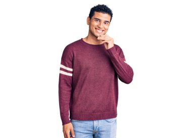 Gündelik kıyafetler giyen İspanyol yakışıklı genç adam kameraya bakıyor kollarını kavuşturup gülümseyerek ve çenesini kaldırarak. Olumlu düşünmek. 