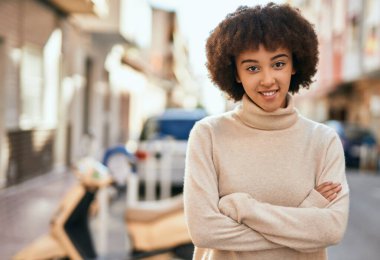 Kollarını kavuşturmuş genç İspanyol kız şehirde mutlu bir şekilde gülümsüyor..