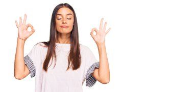 Gündelik kıyafetler giyen, gözleri kapalı gülümseyen genç İspanyol kadın parmaklarıyla meditasyon hareketi yapıyor. yoga konsepti. 