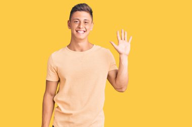 Gündelik kıyafetler giyen genç yakışıklı adam beş numarayı gösterip işaret ederken kendinden emin ve mutlu bir şekilde gülümsüyor.. 