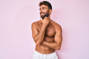 Elleri çenesinde tişörtsüz, soru soran, düşünceli bir İspanyol genç. Düşünceli bir yüzle gülümsüyor. şüphe kavramı. 