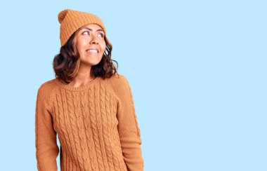 Genç, güzel, melez, yün kazak giyen ve kış şapkalı bir kadın yüzünde gülümseme, doğal bir ifade ile yan yana bakıyor. Kendinden emin gülen. 