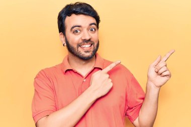 Gündelik kıyafetler giyen genç İspanyol adam gülümseyip kameraya bakıyor ve iki eliyle ve parmaklarıyla kenarı işaret ediyor.. 