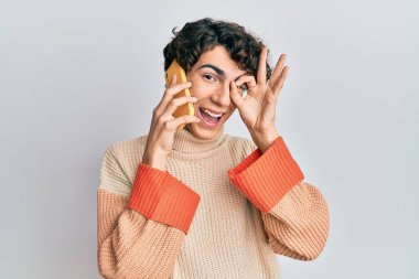 İspanyol genç adam akıllı telefondan konuşuyor gülümsüyor mutlu mesut gülümsüyor el ele imzala parmaklarının arasından bakıyor. 