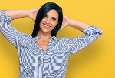 Kafkasyalı genç bir kadın günlük kıyafetler giyiyor rahatlıyor ve esniyor, kolları ve elleri başının arkasında mutlu bir şekilde gülümsüyor. 