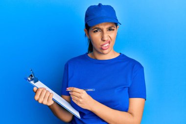 Kurye üniforması giyen güzel esmer kadın elinde dosyasından bihaber ve kafası karışık bir ifade tutuyor. şüphe kavramı. 