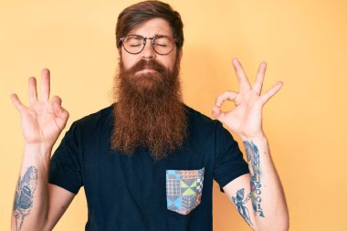 Uzun sakallı, sıradan kıyafetler ve gözlük takan, gözleri kapalı gülümseyen, meditasyon hareketi yapan, uzun saçlı yakışıklı genç adam. yoga konsepti. 