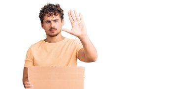 Genç, kıvırcık saçlı, elinde boş pankart tutan, eli açık, dur işareti yapan, ciddi ve kendinden emin ifadeli, savunma jesti 