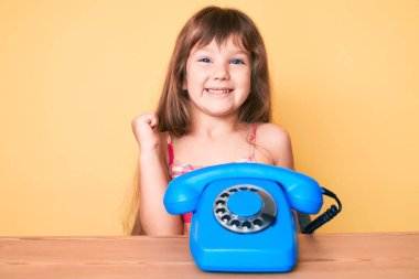 Masada oturan uzun saçlı beyaz kız klasik telefon kullanarak gururla bağırıyor, zaferi kutluyor ve kollarını kaldırarak başarıyı kutluyor. 