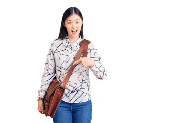 Genç, güzel, Çinli bir kadın evrak çantası tutuyor. Gülümsüyor, mutlu bir şekilde elini ve parmağını gösteriyor. 