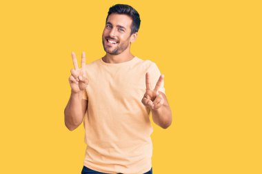 Gündelik kıyafetler giyen genç İspanyol adam kameraya bakıp zafer işareti yaparken parmaklarını gösteriyor. İki numara.. 