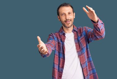 Sıradan kıyafetler giymiş genç yakışıklı bir adam kameraya bakıyor ve sarılmak için kollarını açmış gülümsüyor. Mutluluğu kucaklayan neşeli bir ifade.. 
