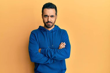 Gündelik kıyafetler giyen, kuşkucu ve gergin genç İspanyol bir adam. Yüzünde çapraz kollarla onaylamayan bir ifade var. negatif kişi. 