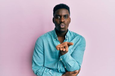 Yakışıklı, sıradan kıyafetler giyen, kameraya bakıp havada el sallayan ve güzel ve seksi bir şekilde öpüşen bir zenci. aşk ifadesi. 