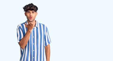 Gündelik giysiler giymiş genç İspanyol bir adam kameraya bakıp havada bir öpücük savuruyor ve sevimli ve seksi oluyor. aşk ifadesi. 