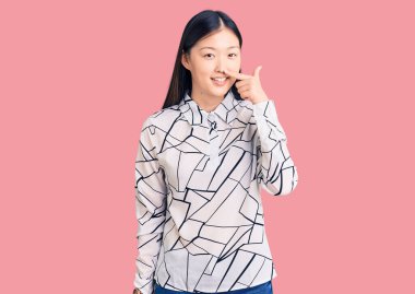 Genç, güzel, Çinli bir kadın, günlük tişörtler giyip, parmaklarıyla yüzünü ve burnunu göstererek neşeli bir şekilde gülümsüyor. güzellik konsepti 