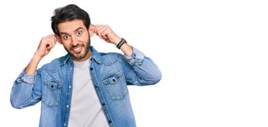 Günlük kıyafetler giyen, gülümseyen, parmaklarıyla kulaklarını çeken genç İspanyol bir adam, komik bir jest. deneme sorunu 