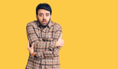 Latin kökenli genç bir adam günlük kıyafetler giyiyor. Kış soğuğu için titriyor ve donuyor. Yüzünde üzgün ve şok ifadesi var. 