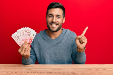 Yakışıklı ispanyol adam İsrail şekellerini tutuyor gülümsüyor mutlu bir şekilde elini ve parmağını yana doğru gösteriyor 