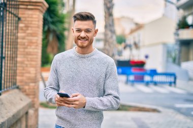Beyaz adam şehirde akıllı telefon kullanarak mutlu bir şekilde gülümsüyor..