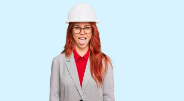 Genç kızıl saçlı kadın mimar şapkası takıyor ve komik bir ifadeyle dilini dışarı çıkarıyor. duygu kavramı. 